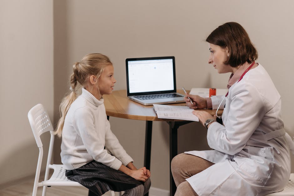 Doctor in lab coat consulting a young girl in a clinic with a laptop on the table.