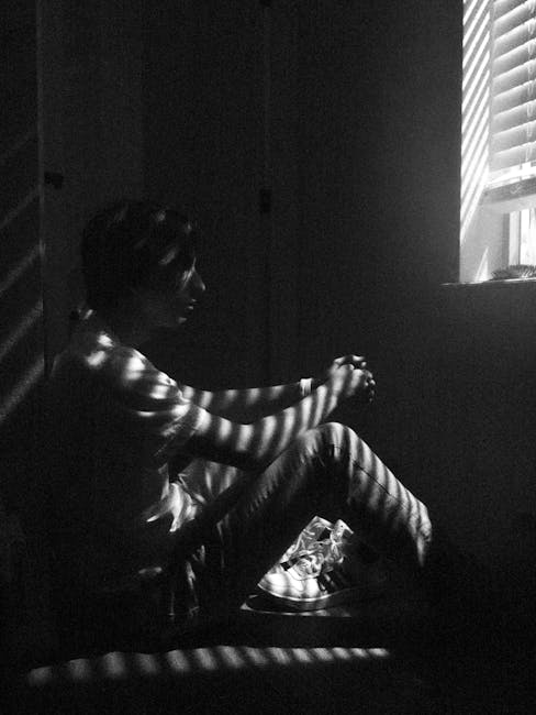 pexels-photo-3244604-3244604 Black and white photo of a thoughtful man sitting by a window with blinds casting shadows.