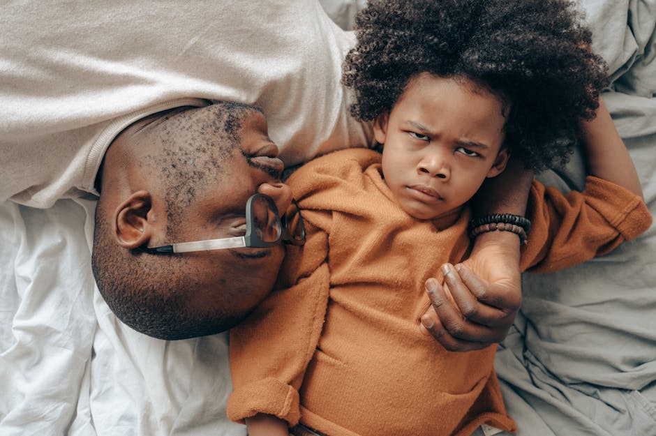 pexels-photo-4546116-4546116 Top view of African American man in glasses lying near angry child in casual clothes while cuddling together in comfortable bedroom