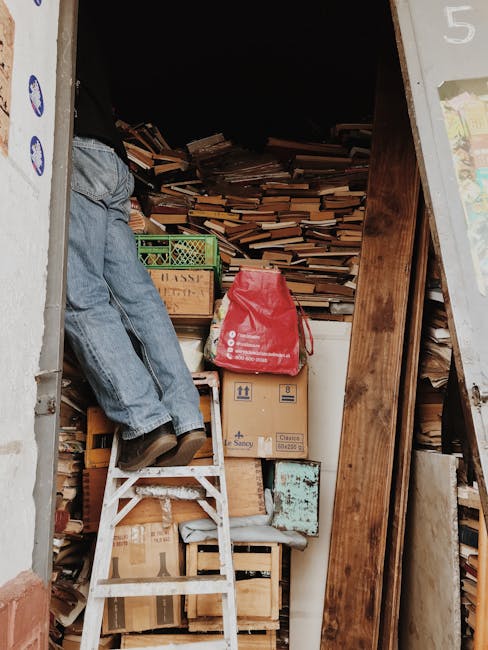 pexels-photo-8826970-8826970 A person climbing a ladder in a cluttered storage area filled with books and boxes.